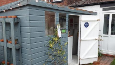 A blue shed with a white door and a string of lights along the roof