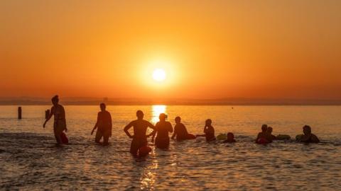 Swimmers in the sea with an orange sky and sun shining in the background