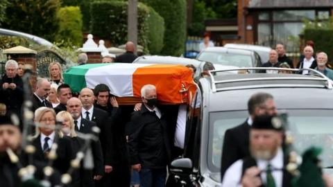 Crowd carrying coffin wrapped in Tricolor orange white and green with funeral procession