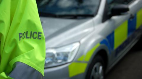 Police officer's arm in a hi-vis jacket with a police car behind