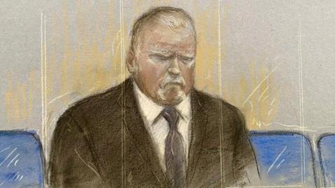 Courtroom sketch showing Robert Bush seated alone behind a glass front shown as vertical sketch marks in beige and white. He is wearing a dark suit, white shirt and dark tie. The illustration is rendered in pastel and pencil tones, with blue courtroom seats visible on either side of the figure. He is positioned centrally against a pale grey background.