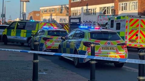 Several emergency police cars and vans and ambulances parked on a road.
A cordon has been put up
