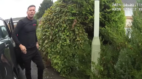 A screen-grab of a police body-cam video shows Steven Luck, who has short brown hair and a beard, exiting a black car onto a residential street.