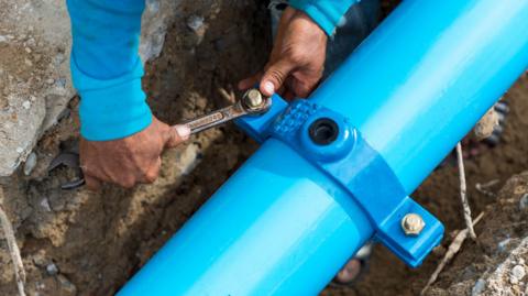 A man fixes a blue pipe under the ground