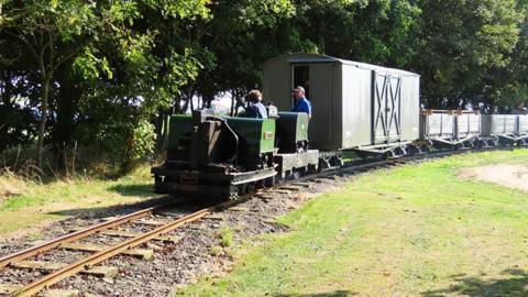 Locomotive with two crew pulling olive wagons dating back to World War One