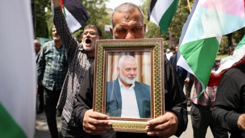 A man carries a photo of Ismail Haniyeh among a wave of Palestinian flags during a protest in Tehran