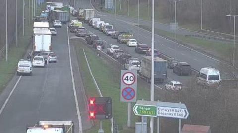 A traffic camera shows vehicles queuing on a junction joining a dual carriageway. A sign showing Bangor in one direction and Conwy in another can be seen in the foreground. 