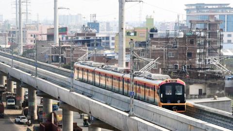 A metro train runs along a bridge over a street with buildings and the city skyline in the background as the first Patnat metro train is tested in Patna in September.