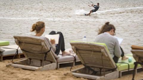 Two European holidaymakers lie on sunloungers in Western Sahara, while another kite surfs in the sea