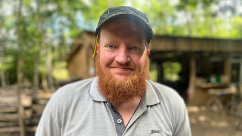 Dan wears a dark cap, he has a pencil tucked into his ear and a long ginger beard.