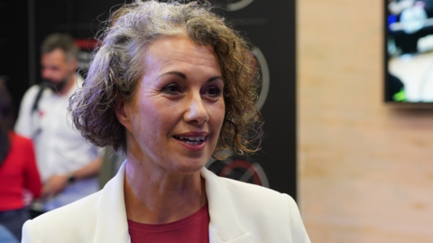 Sarah Champion MP wears a white jacket and a red t-shirt