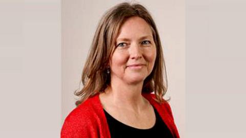 Mandy Clare is smiling. She has long brown hair and is wearing a black top and red cardigan.