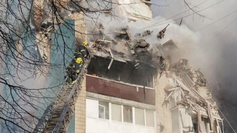 Rescuers at the top of a ladder work at the site of the apartment building damaged by strikes, the building is damaged and smoking and the rescuers wear emergency gear, in Ternopil on Wednesday. 