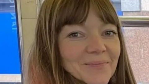 A woman with long light brown hair, smiles at the camera.