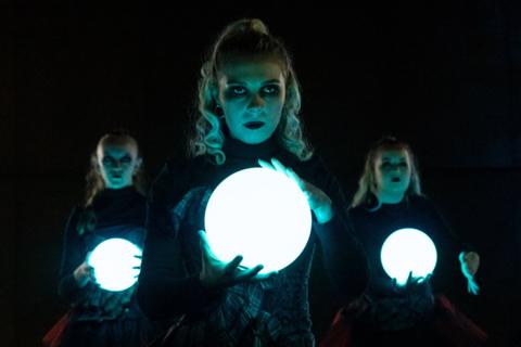 three ladies stand holding illuminated globes. They are in front of a dark background