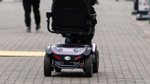 Rear view of the bottom of a mobility scooter riding along a cobbled walkway