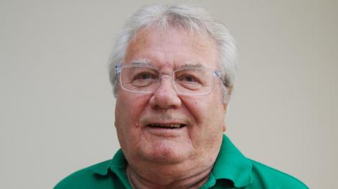 Peter Bridges with short white hair and glasses wearing a green tee shirt