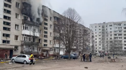 Smoke rises from a building as officials stand around nearby.