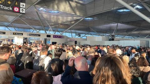 Lots of people are crowded together inside Stansted Airport. 