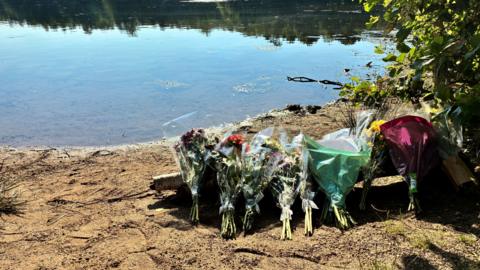 Bouquets of flowers left on sand by a lake. 