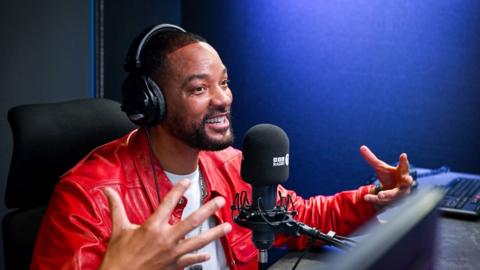 Will Smith, wearing a red leather jacket, gesticulating in the Radio 1Xtra studio