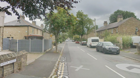 A residential street with trees and cars parked on one side 