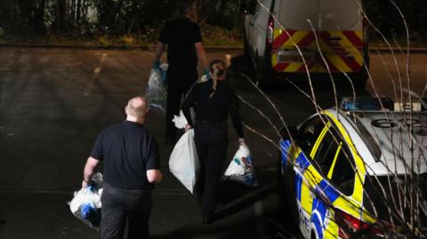 Three police officers walked towards two marked police vehicles with bags of evidence