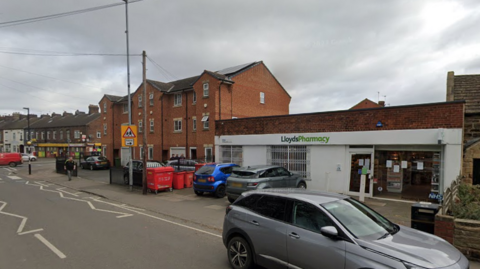 A semi-residential street with a pharmacy and a number of parked cars