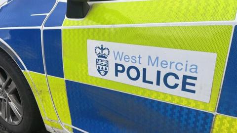 A white West Mercia Police sticker on a yellow and blue police car.