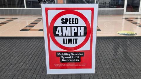 A sign in the window of Idlewells Shopping Centre which shows 4mph, and says "mobility scooter speed limit awareness"