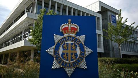 Outside Durham Police headquarters, with a close-up of blue sign which says Durham Constabulary and has a four lions symbol as well as the crown. 