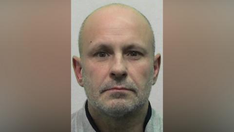 Mugshot of Adams. He is bald with a grey stubbly beard.
