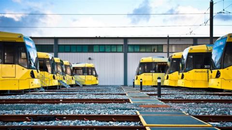 Nine bright yellow Metrolink trams stationary in a depot.