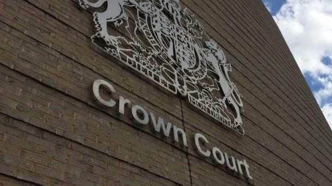 A close up view of the criminal courts crest and the words "crown court" on the Cambridge Crown Court building. It is a light coloured brick building. 