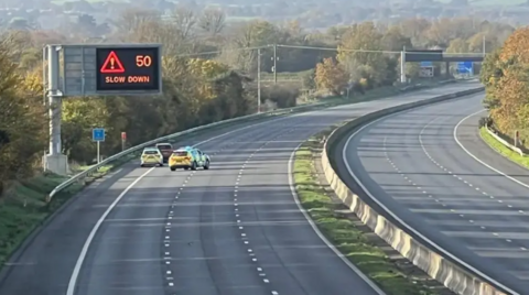 A closed motorway with two police cars and a regular car parked near the hard shoulder