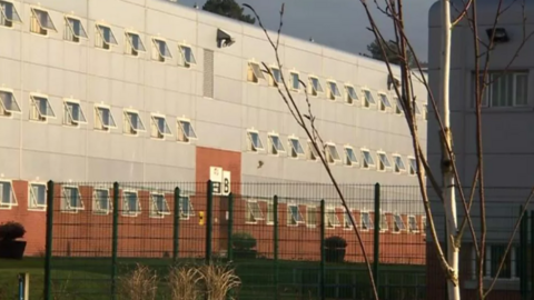 Parc prison, a building of red brick on the lower floor and silver metal cladding above, as seen from behind a green metal fence