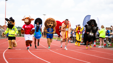 Seven people all dressed in different costumes, competing in a track running race.
