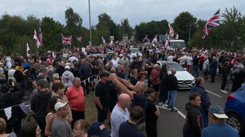 A large crowd of people, many waving flags and standing in the road. 