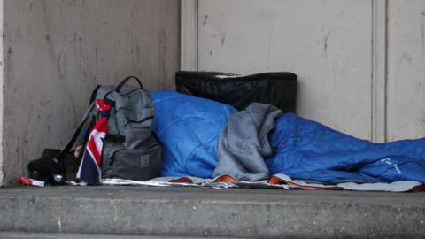 Someone in blue sleeping bag, rough sleeping, with grey backpack.