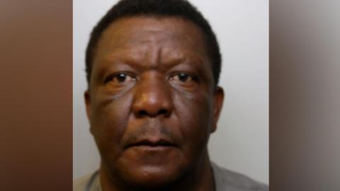Custody image of Francis Siyachitema,. He is wearing a grey top and has a neutral expression.