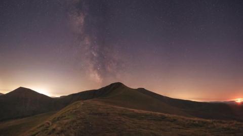 The Milky Way over Pen y Fan from the north ridge. Three peaks are visible against yellow and purple skies