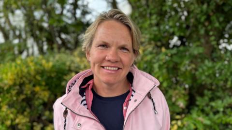 A picture of Deputy Sasha Kazantseva-Miller. She is wearing a pink jacket and has blonde hair.