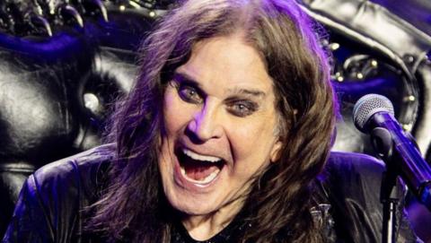 Ozzy Osbourne on stage with his arms outstretched and a big open-mouthed grin