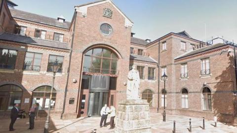 The outside of a multiple-storey, brick court building, with a statue in the centre of the courtyard.