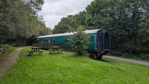 A disused green railway carriage by a fence.