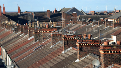 A shot of a row of terraced house roofs, with chimneys, aerials and satellite dishes on display. 