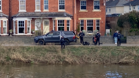 Rescue crews stand by the riverbank in Diglis. Members of the public watch as crews use equipment from a vehicle.