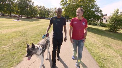 One man walks alongside another walking a dog