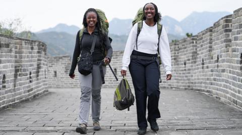 Two young women with large rucksacks and in hiking boots walk down the Great Wall of China