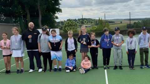 Young members of Mexborough Tennis Club pose for a photograph on a tennis court with an adult